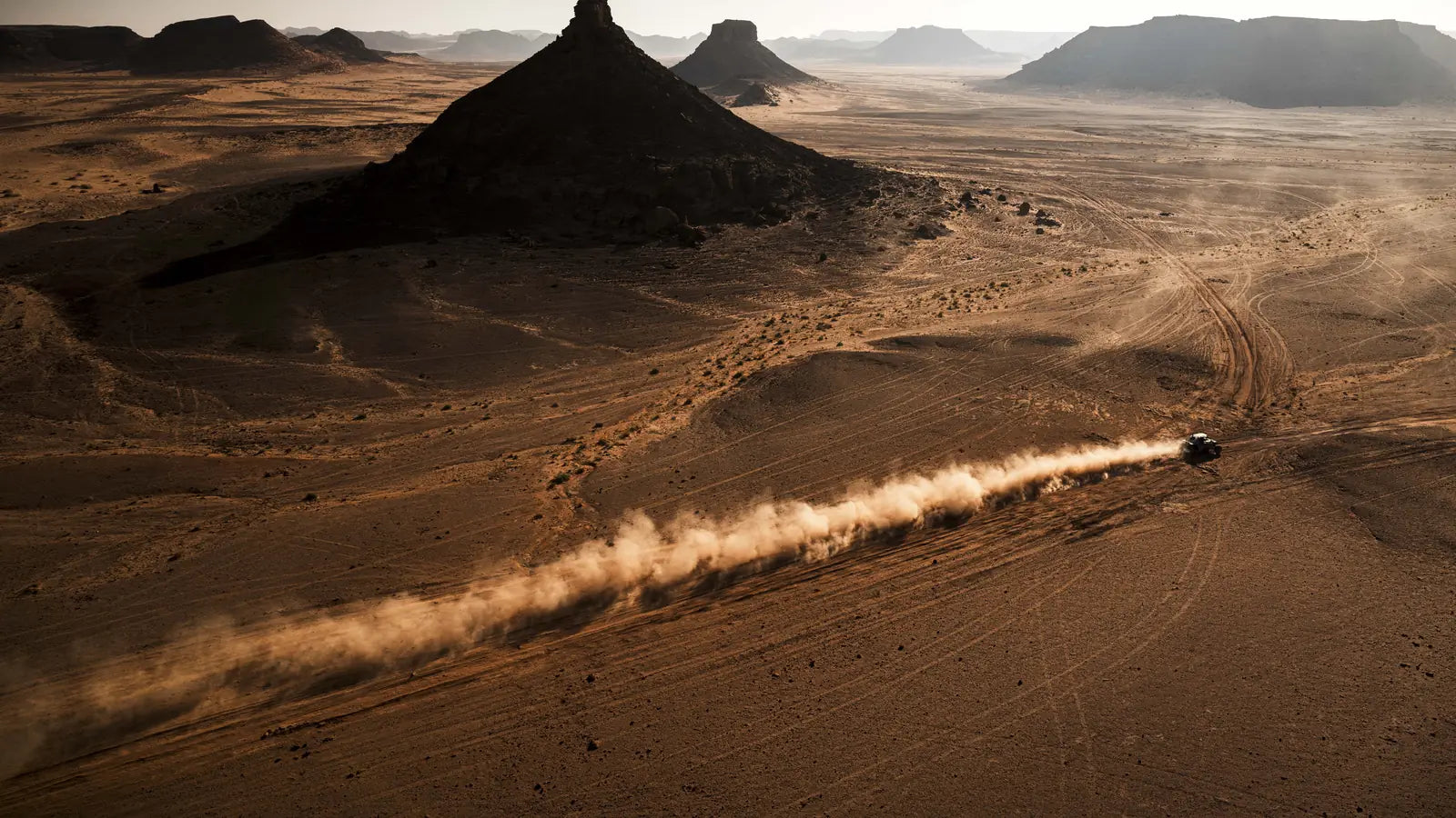 Pico rochoso isolado e rasto de poeira de um concorrente no deserto. Foto © A.S.O. / C. Lopez
