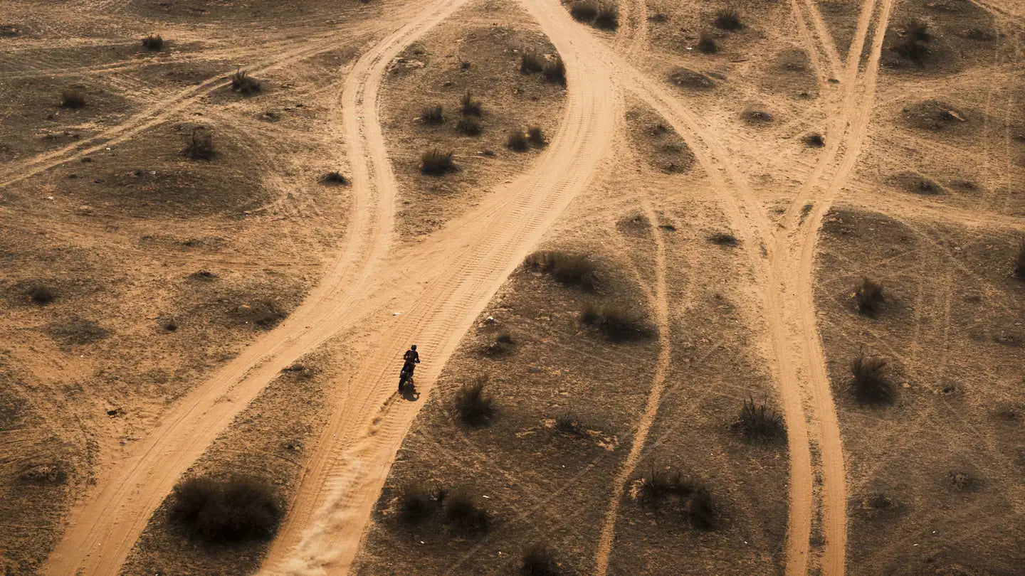 Trilhos cruzados na areia vistos de cima, com um motociclista. Foto © A.S.O. / C. Lopez